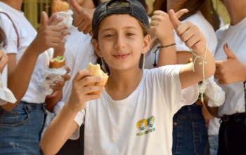 Un ragazzo fa il pollice in su mentre gusta del cibo in una scuola in Siria.