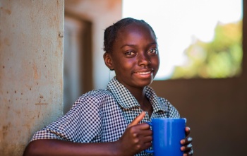 Una ragazza con una tazza di cibo in una scuola in Zambia.