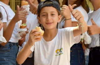 Un ragazzo fa il pollice in su mentre gusta del cibo in una scuola in Siria.