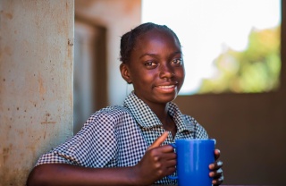 Una ragazza con una tazza di cibo in una scuola in Zambia.