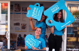 I volontari posano con grandi tazze in un evento di Mary's Meals.