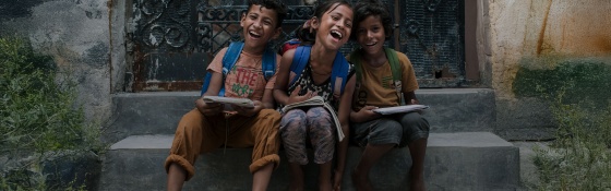 Three children sitting on some steps laughing and smiling looking towards the camera.
