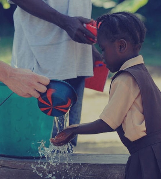 Un volontario lava le mani di un bambino a scuola.