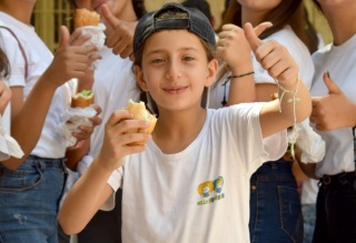 Un ragazzo fa il pollice in su mentre gusta del cibo in una scuola in Siria.
