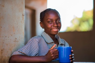Una ragazza con una tazza di cibo in una scuola in Zambia.